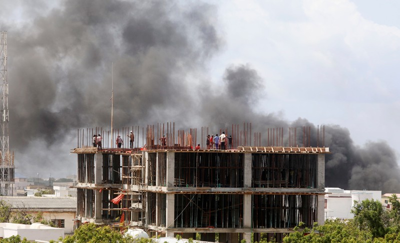 Workers are seen on a construction site as smoke billows from the scene of an explosion in Mogadishu