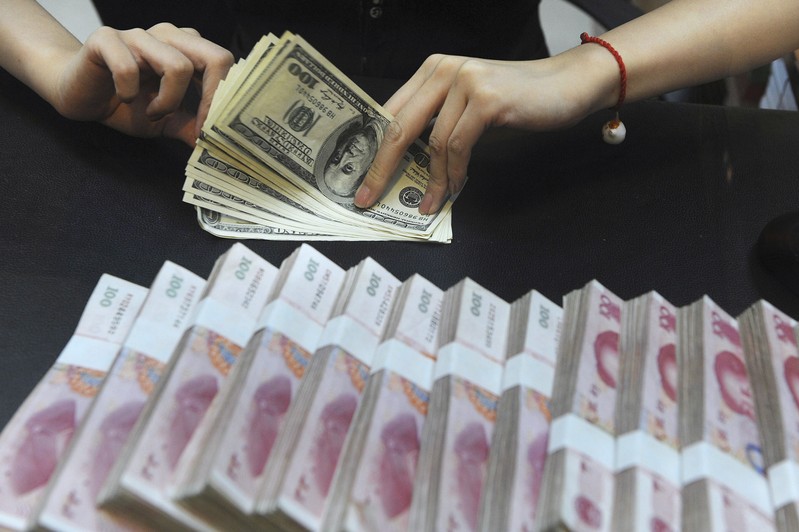 File photo of an employee counting U.S. dollars next to yuan banknotes at a bank in Hefei