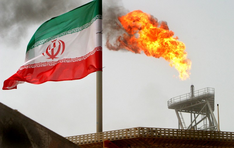 A gas flare on an oil production platform in the Soroush oil fields is seen alongside an Iranian flag in the Persian Gulf