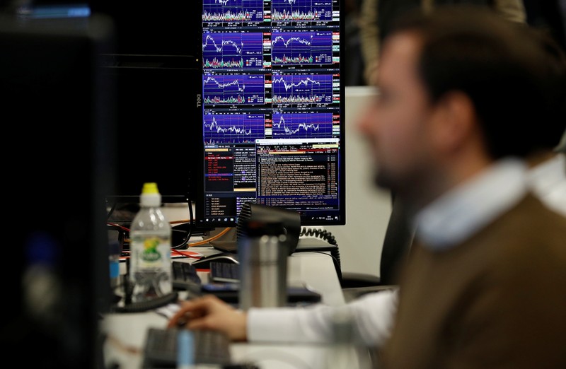 FILE PHOTO: Financial traders work at their desks at CMC Markets in the City of London