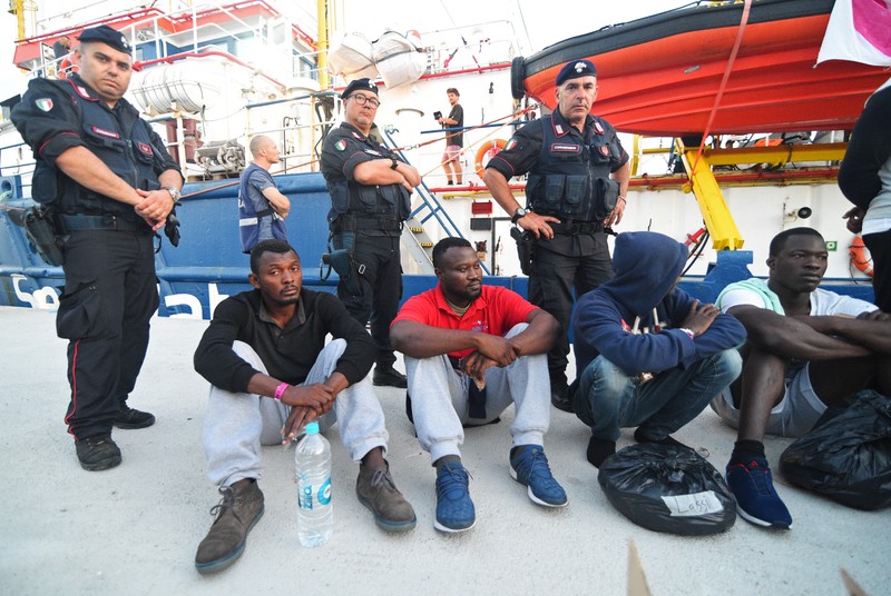 Italian policemen stand next to migrants after they disembarked from the Sea-Watch 3 rescue ship in Lampedusa