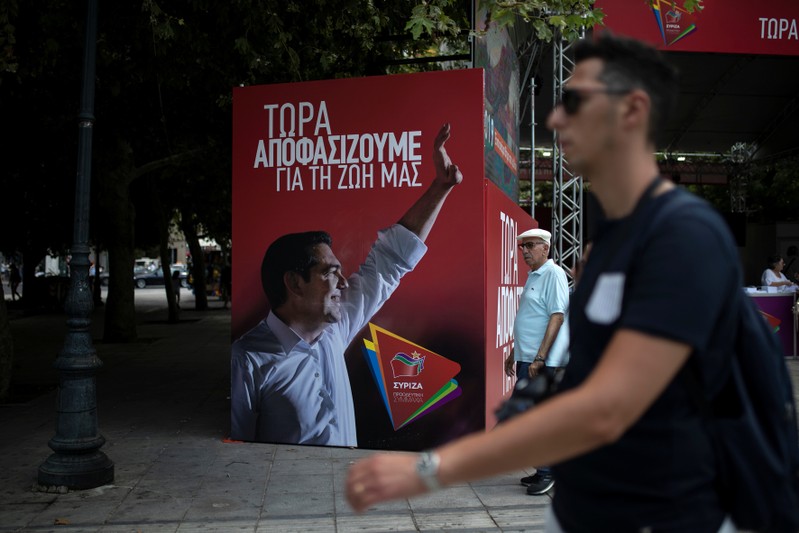 People walk past a poster depicting Greek PM Tsipras at the election kiosk of the leftist Syriza party in Athens