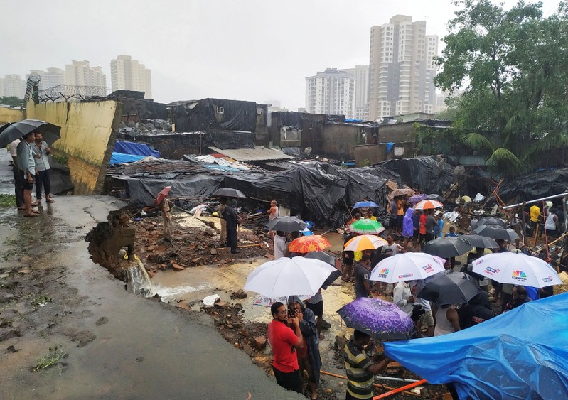 People stand among the debris after a wall collpased on hutments due to heavy rains in Mumbai