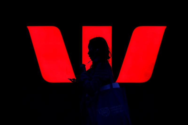 A woman walks past an illuminated logo for Australia's Westpac Bank in Sydney