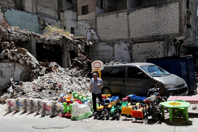 FILE PHOTO: A street vendor sells toys next to rubble of damaged buildings in the city of Idlib