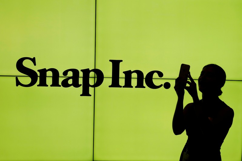 FILE PHOTO: A woman stands in front of the logo of Snap Inc. on the floor of the New York Stock Exchange (NYSE) while waiting for Snap Inc. to post their IPO, in New York City