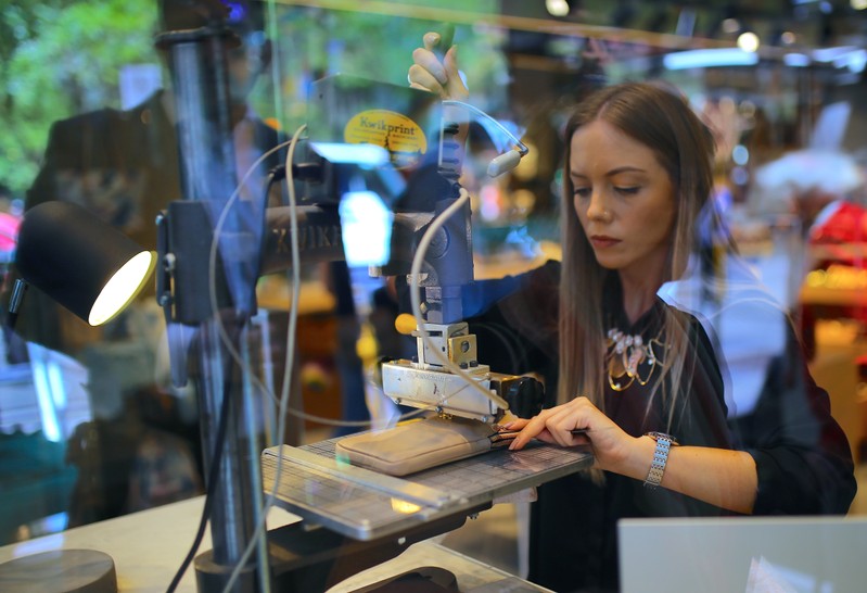 A woman uses a machine to emboss a wallet in the window of a retail store selling leather goods in central Sydney