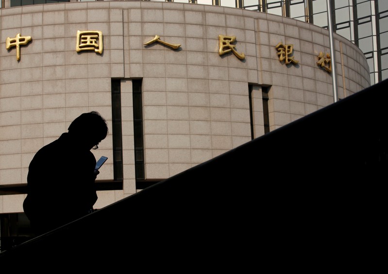 FILE PHOTO: Man sits in front of the headquarters of the People's Bank of China, the central bank, in Beijing