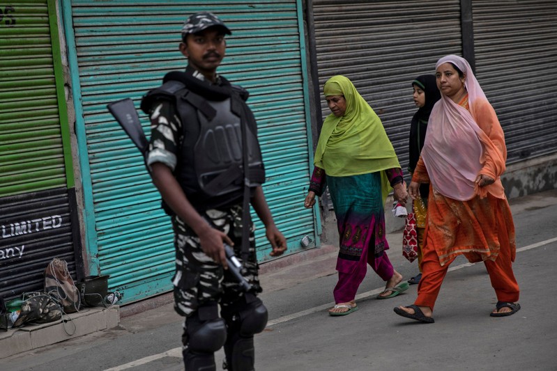 Kashmiri women walk past an Indian security personnel during restrictions after the scrapping of the special constitutional status for Kashmir by the government, in Srinagar
