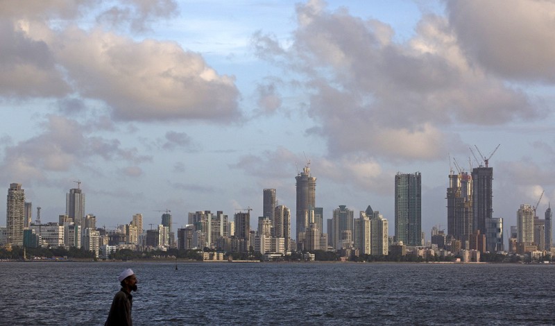 FILE PHOTO - A man walks at the seafront as scattered clouds are seen over Mumbai's skyline