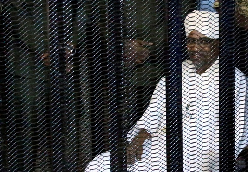 FILE PHOTO: Sudan's former president Omar Hassan al-Bashir sits guarded inside a cage at the courthouse where he is facing corruption charges, in Khartoum