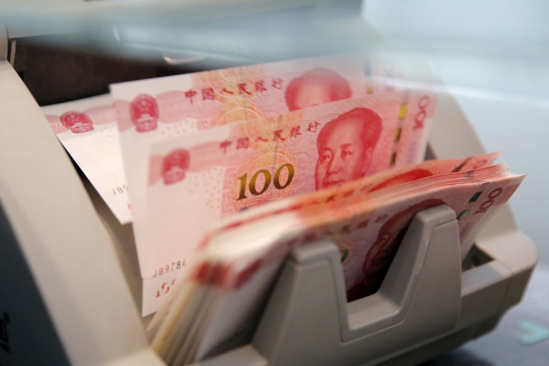 FILE PHOTO: Chinese 100 yuan banknotes in a counting machine while a clerk counts them at a branch of a commercial bank in Beijing