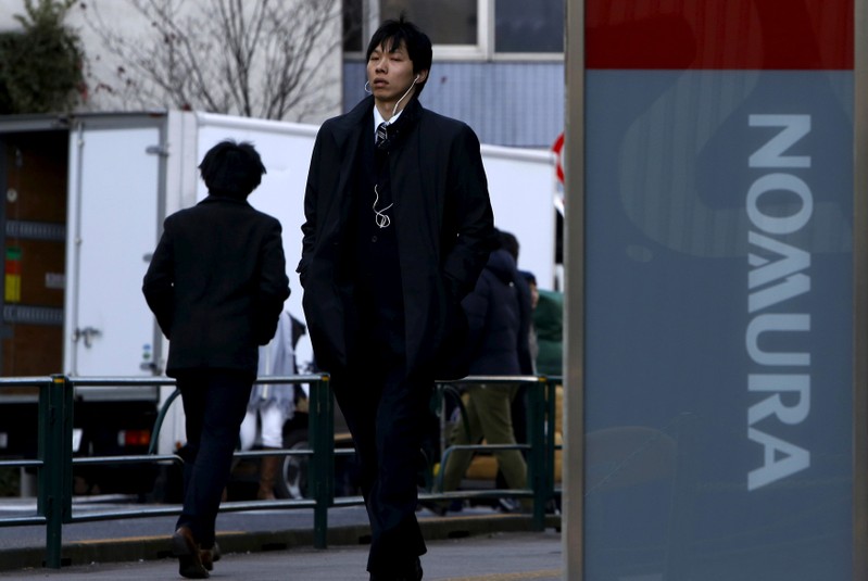 FILE PHOTO: A man walks past a signboard of Nomura Securities outside its branch in Tokyo