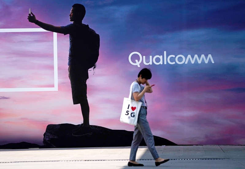 FILE PHOTO: A woman walks past a sign advertising Qualcomm at Mobile World Congress (MWC) in Shanghai