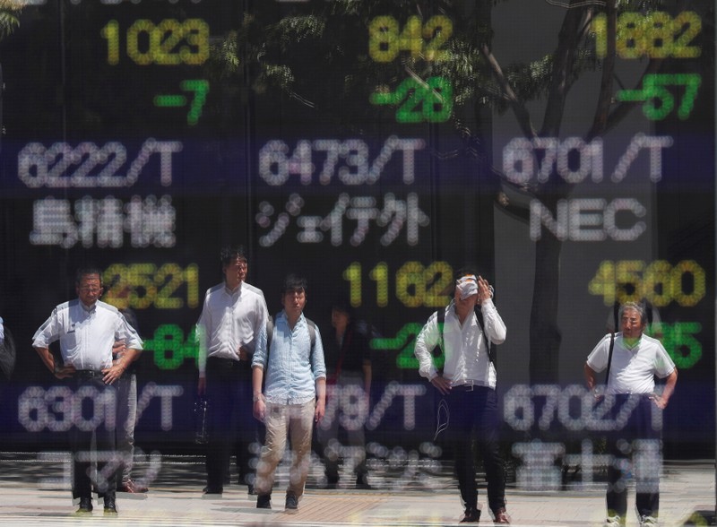 Passersby are reflected on a stock quotation board outside a brokerage in Tokyo