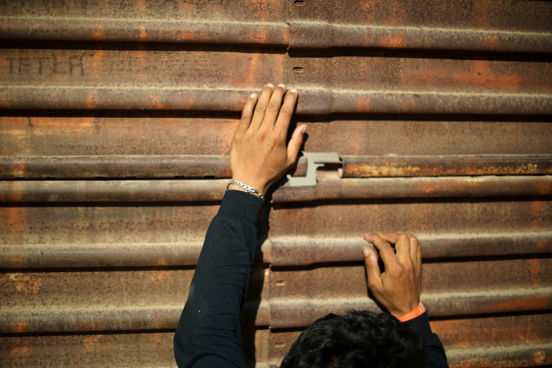 FILE PHOTO: A migrant, part of a caravan of thousands traveling from Central America en route to the United States, tries to look at U.S. border patrol officers through a hole in the border wall between the U.S and Mexico in Tijuana