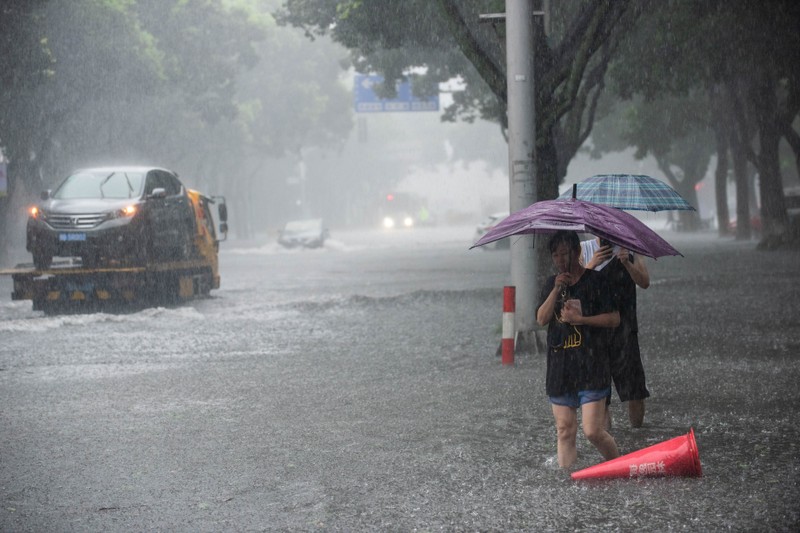 People holding umbrellas wade through floodwaters amid heavy rainfall on a street after super typhoon Lekima made landfall in Ningbo