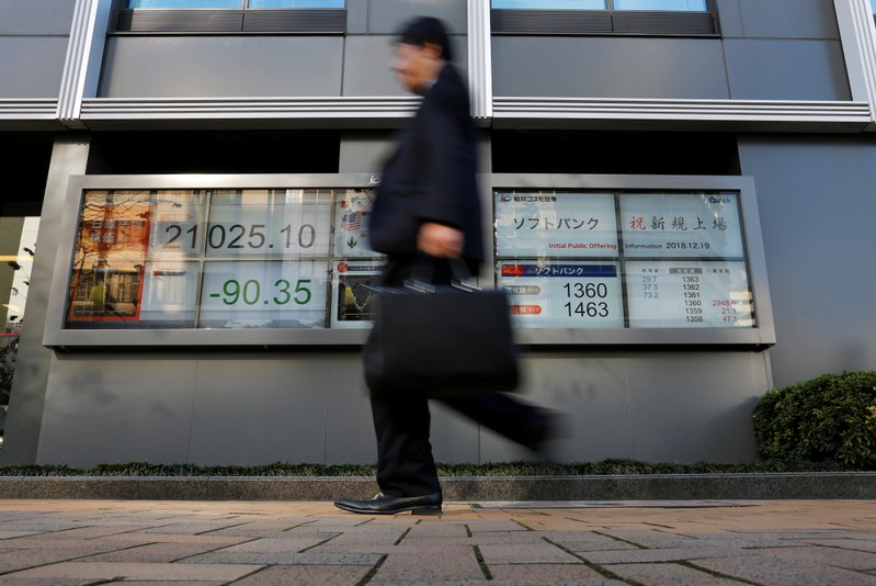 A man walks past in front of a stock quotation board showing the price of the SoftBank Corp. and Nikkei share average outside a brokerage in Tokyo