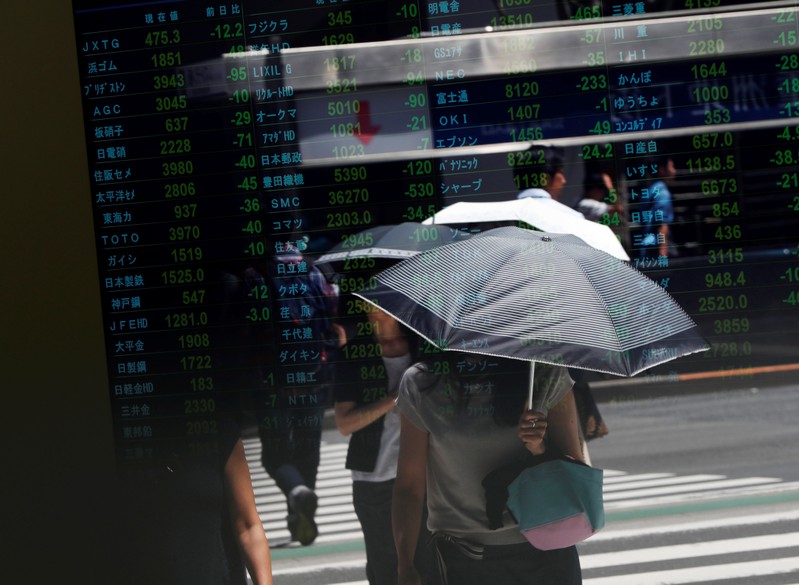 FILE PHOTO - Passersby are reflected on a stock quotation board outside a brokerage in Tokyo