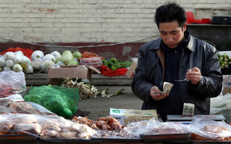 FILE PHOTO: Fruit and vegetables can be seen behind a man selling pork as he checks his money at a small roadside market in central Beijing