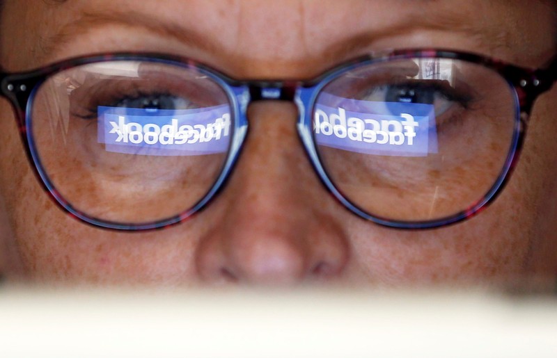 The Facebook logo is reflected on a woman's glasses in this photo illustration