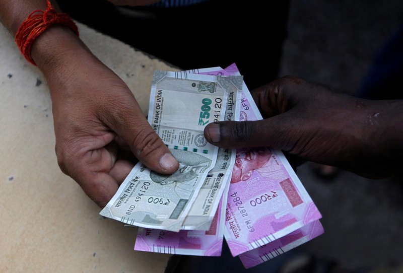FILE PHOTO - A customer hands Indian currency notes to an attendant at a fuel station in Mumbai