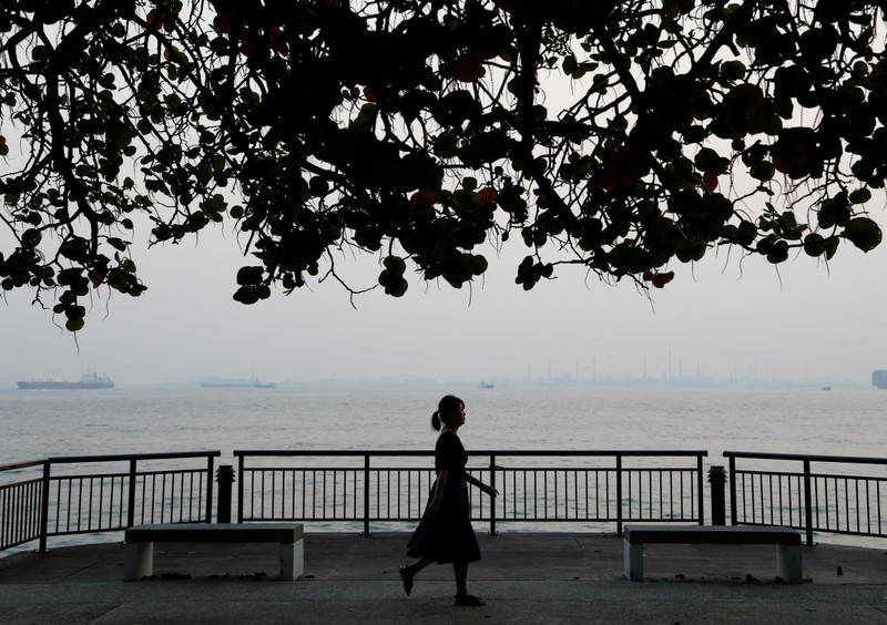 A woman walks past the coastline shrouded by haze in Singapore