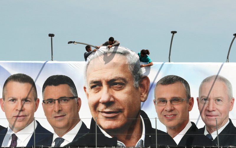 FILE PHOTO: Labourers work on hanging up a Likud election campaign banner depicting Israeli Prime Minister Benjamin Netanyahu with his party candidates, in Jerusalem