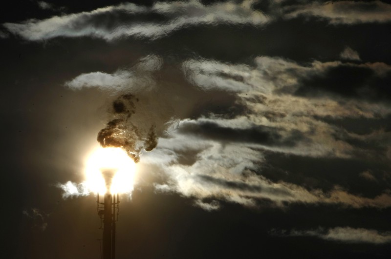 FILE PHOTO: A flare stack emitting fire is silhouetted against the sun at an oil refinery in Melbourne