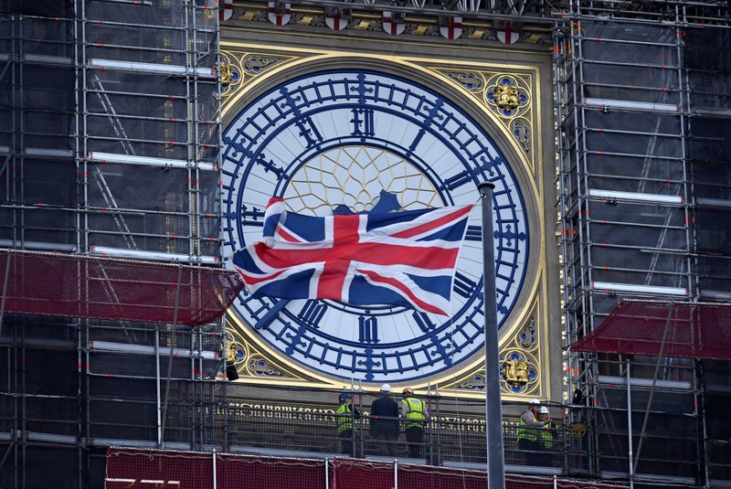 A Union Jack flag flutters in front of Big Ben as workers inspect one of its clocks, in London