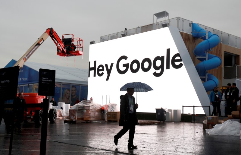 FILE PHOTO: A man walks through light rain in front of the Hey Google booth under construction at the Las Vegas Convention Center in preparation for the 2018 CES in Las Vegas