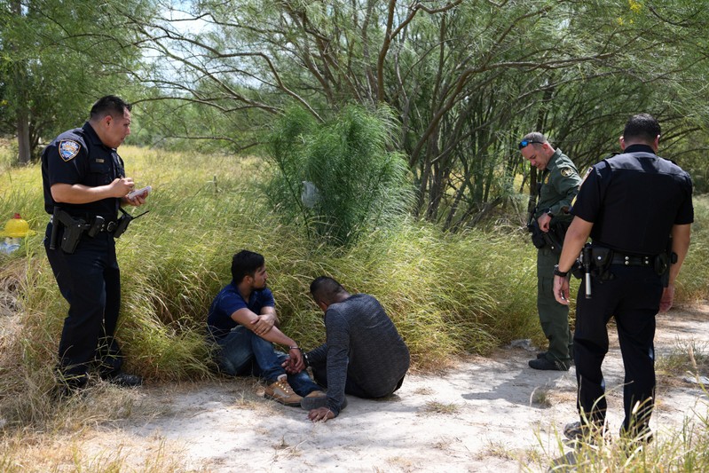 FILE PHOTO: Migrant men sit on the ground after being detained by law enforcement for illegally crossing the Rio Grande and attempting to evade capture in Hidalgo