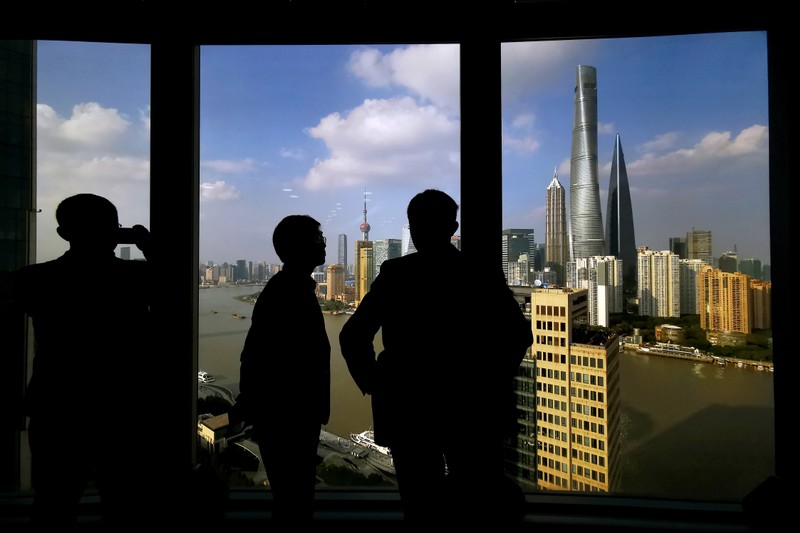 People stand near a window overlooking the financial district in Shanghai