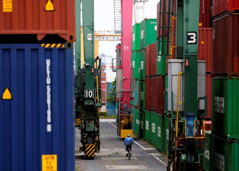 FILE PHOTO: A man in a bicycle drives past containers at an industrial port in Tokyo