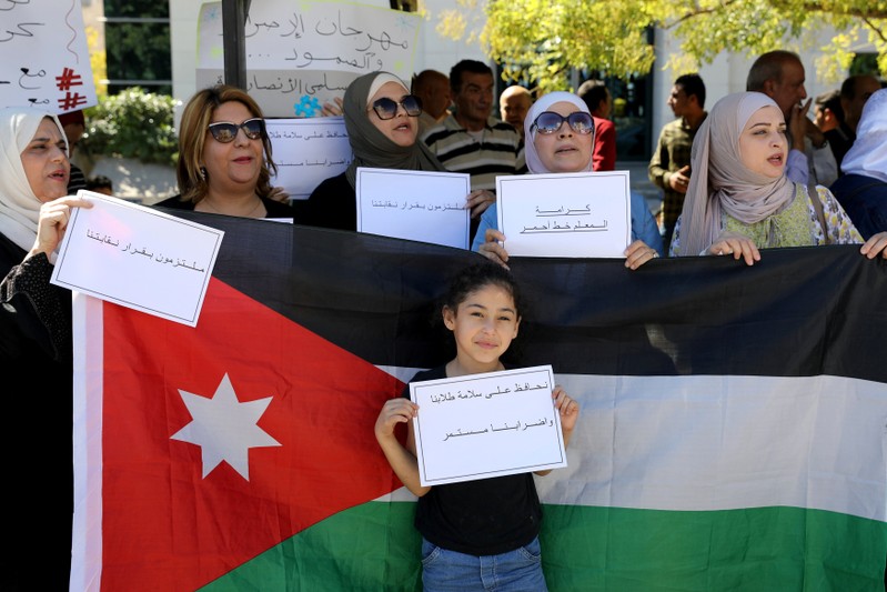 FILE PHOTO: A girl holds placard in front of a Jordanian national flag as public schools' teachers take part in a protest in Amman