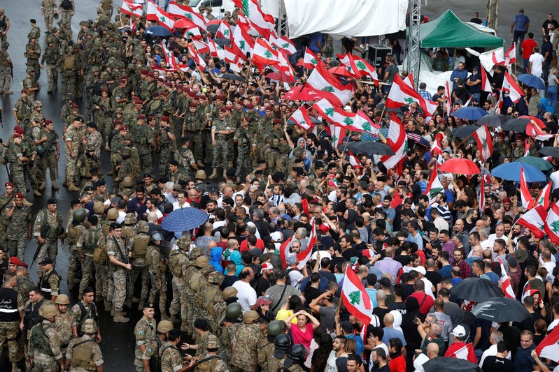 Lebanese army soldiers stand guard next to demonstrators during ongoing anti-government protests at a highway in Jal el-Dib