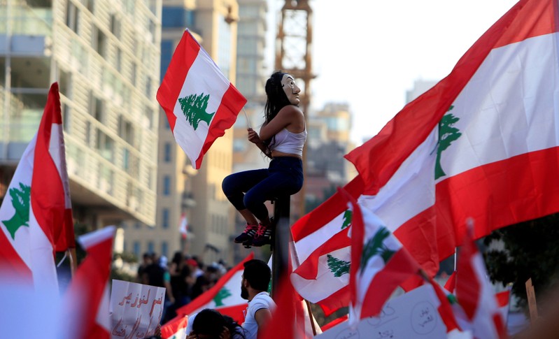 A demonstrator sits on a pole while carrying a national flag during an anti-government protest in downtown Beirut