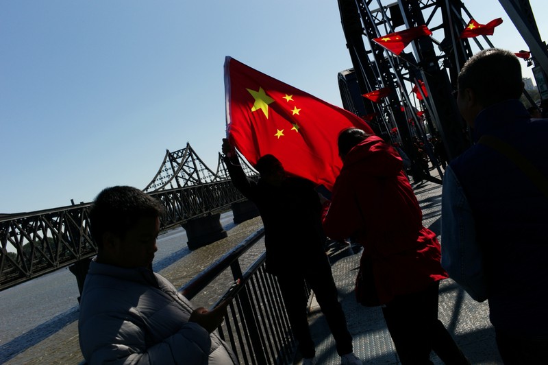 Chinese visitor poses for picture with a Chinese flag on the Broken Bridge near the Friendship Bridge which connects North Korea's Sinuiju and China over the Yalu river, in Dandong