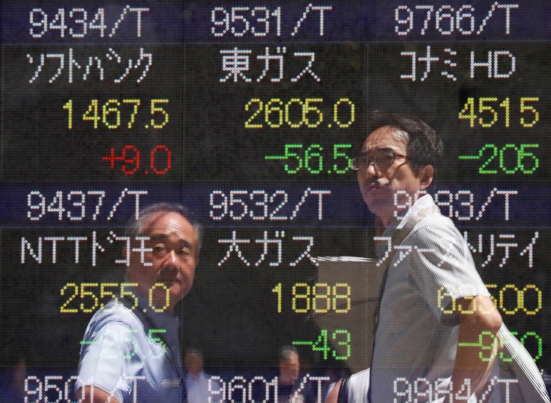 Passersby are reflected on a stock quotation board outside a brokerage in Tokyo