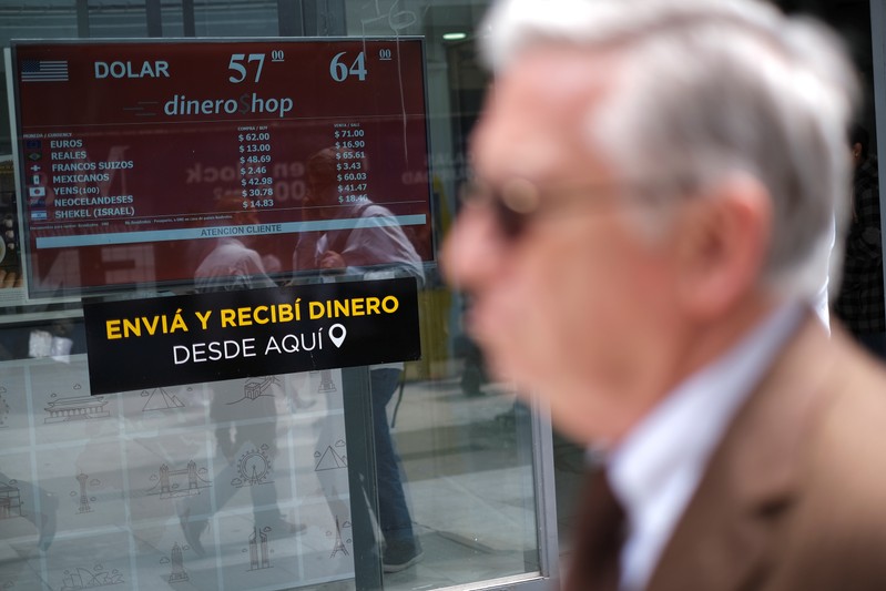 People walk past a screen showing currency exchange rates at a currency exchange shop in Buenos Aires