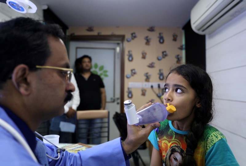 Dr. Dhiren Gupta, a pediatrician, demonstrates to his patient Akshra Quereshi how to use a spacer device for her medication at a hospital in New Delhi
