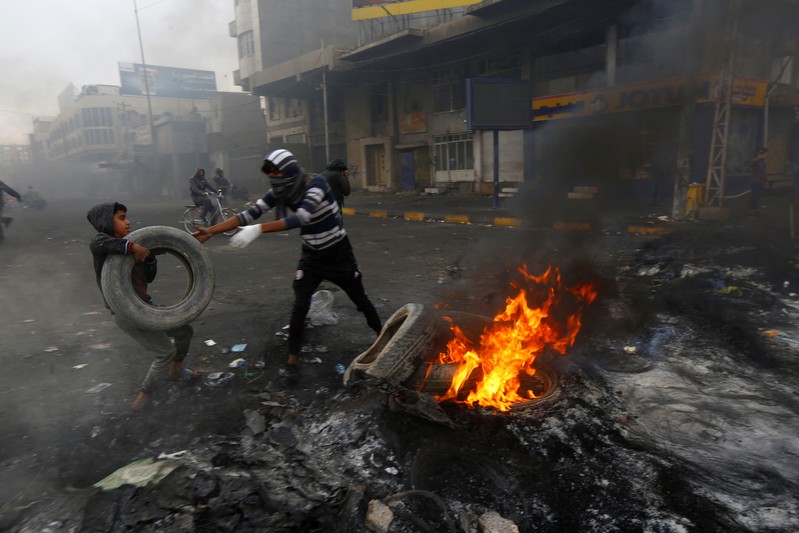 Iraqi demonstrators burn tires to block a street during ongoing anti-government protests in Najaf