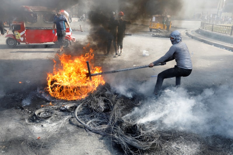 An Iraqi demonstrator pulls a burnt tire as he blocks the road during ongoing anti-government protests, in Baghdad