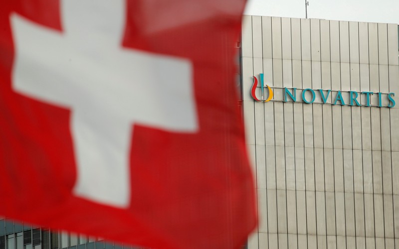 FILE PHOTO: Switzerland's national flag flies in front of the logo of Swiss drugmaker Novartis in Basel