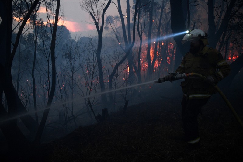 A NSW Rural Fire Service firefighter conducts property protection as a bushfire burns close to homes on Railway Parade in Woodford NSW