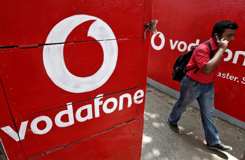 FILE PHOTO: Man speaks on his mobile phone as he walks past the logos of Vodafone painted on a roadside wall in Kolkata
