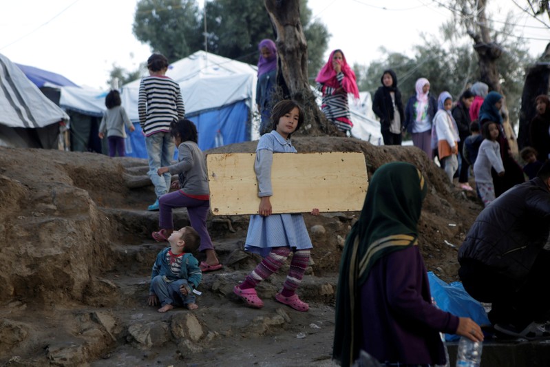 FILE PHOTO: A girl carries a wooden board as she makes her way at a makeshift camp for refugees and migrants next to the Moria camp, on the island of Lesbos