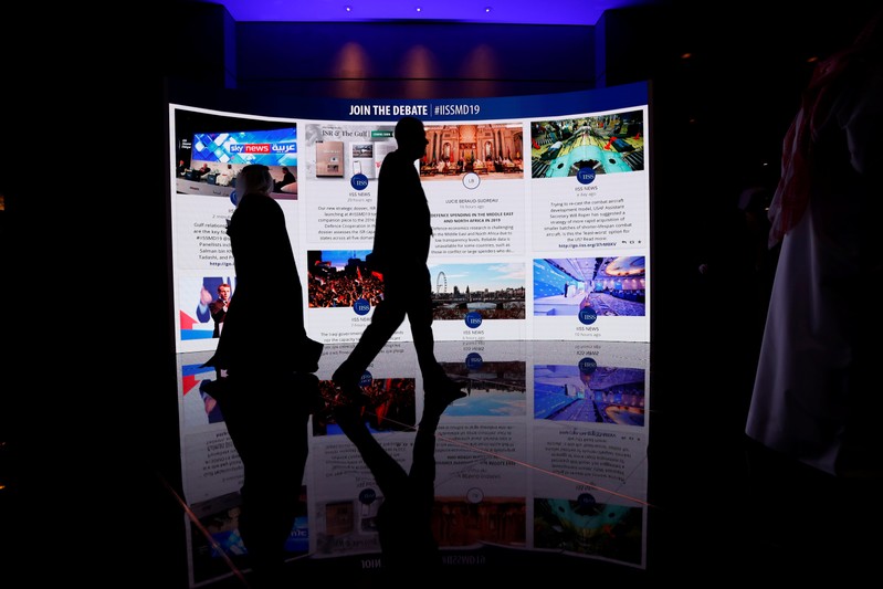 Visitors pass in front of an advertisement screen at the 15th Regional Security Summit IISS Manama Dialogue 2019, in Manama