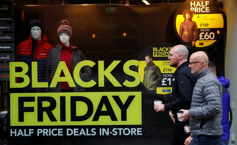 People walk past a sign advertising Black Friday offers in the window of a Blacks outdoor clothing store in Manchester, Britain