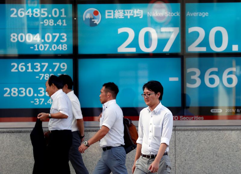 Men walk past in front of an electric screen showing Japan's Nikkei share average outside a brokerage in Tokyo
